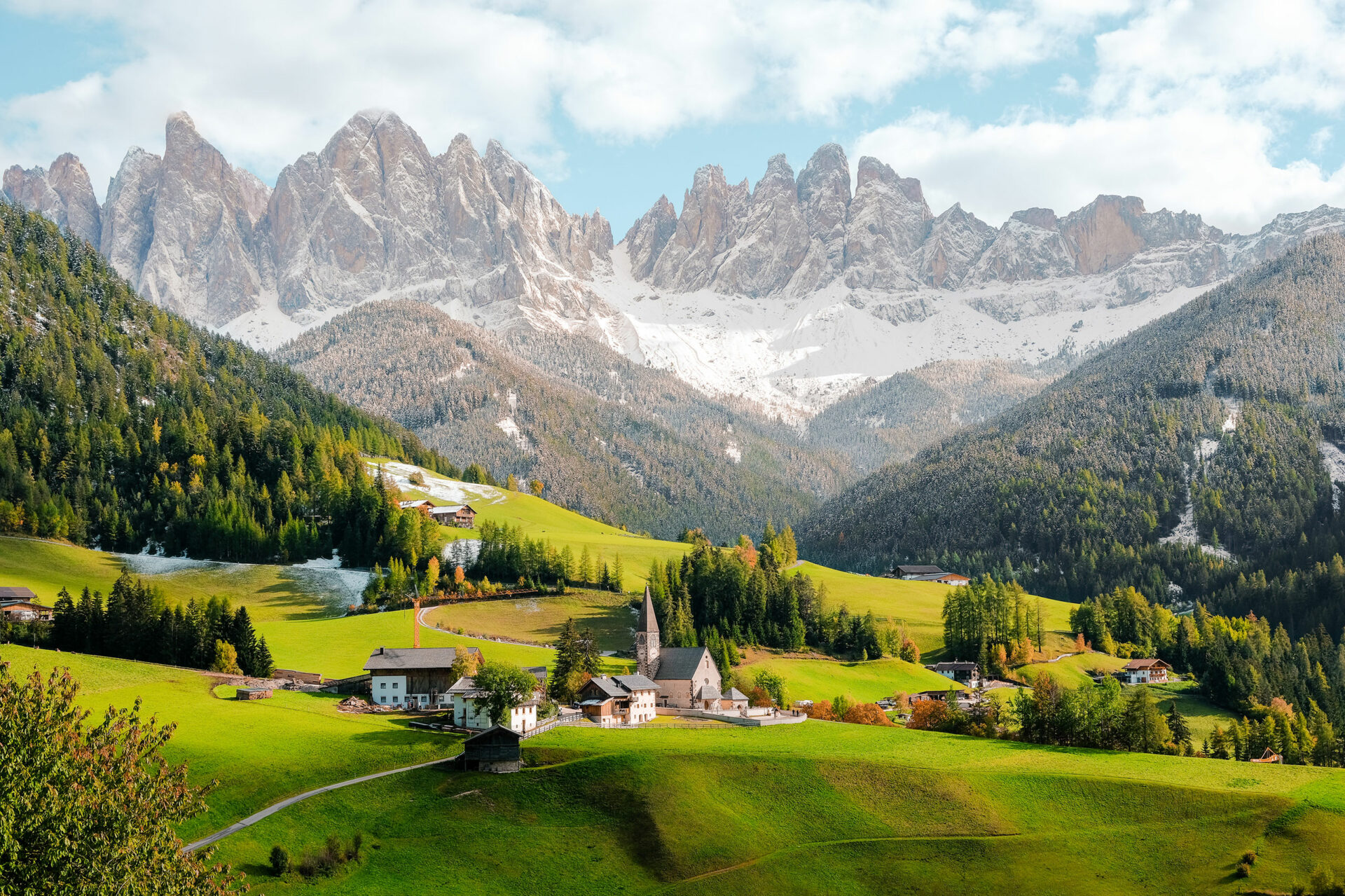 cluster of village homes on green pastures with snowy mountains in the background